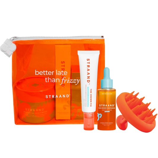 A collection of hair care products including a pre-wash scalp oil, a scalp serum, and a scalp brush, packaged in a bright orange translucent bag with 'better late than frizzy' text, and a small orange sun-shaped accessory.
