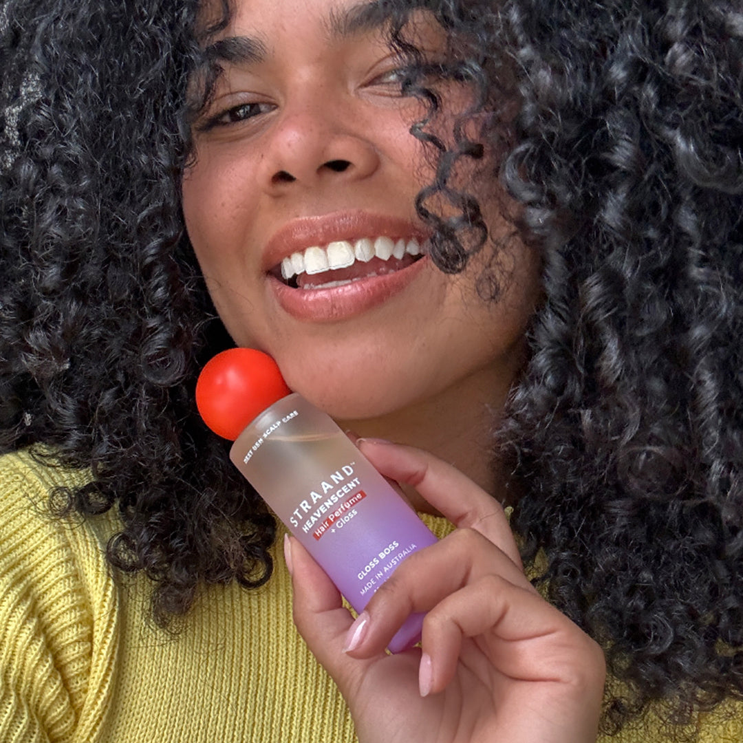 Woman with dark curly hair smiling while holding the hair perfume