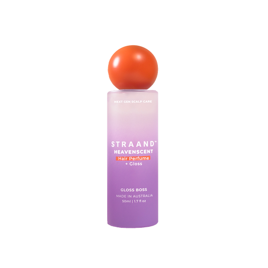A bottle of HeavenScent Hair Perfume + Gloss with a purple label and a orange cap, indicating it is a hair care product.