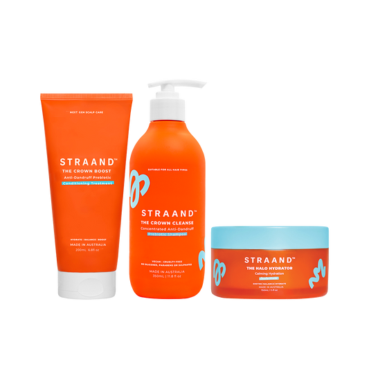 A set of three orange-colored hair care products from the brand STRAAND, including a shampoo, a conditioning treatment, and a scalp mask.