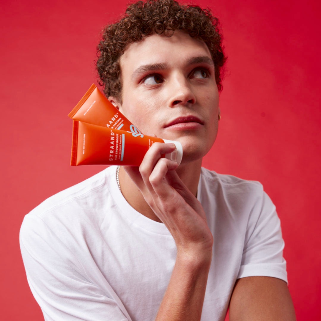 Man with curly hair on red background holding mini orange bottles of shampoos