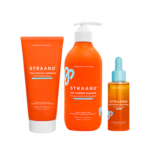 A set of three orange-colored hair care products from STRAAND, including a pre-wash scalp oil, a crown cleanse shampoo, and a miracle worker exfoliating scalp scrub.