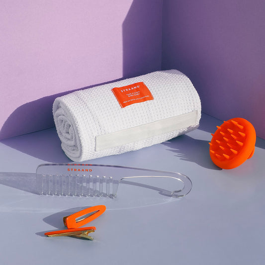 Rolled white hair towel with hair comb, a scalp brush that is orange and some bright orange hair clips.
